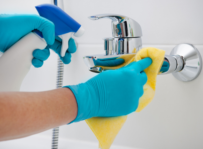 woman doing chores in bathroom, cleaning faucet with spray detergent