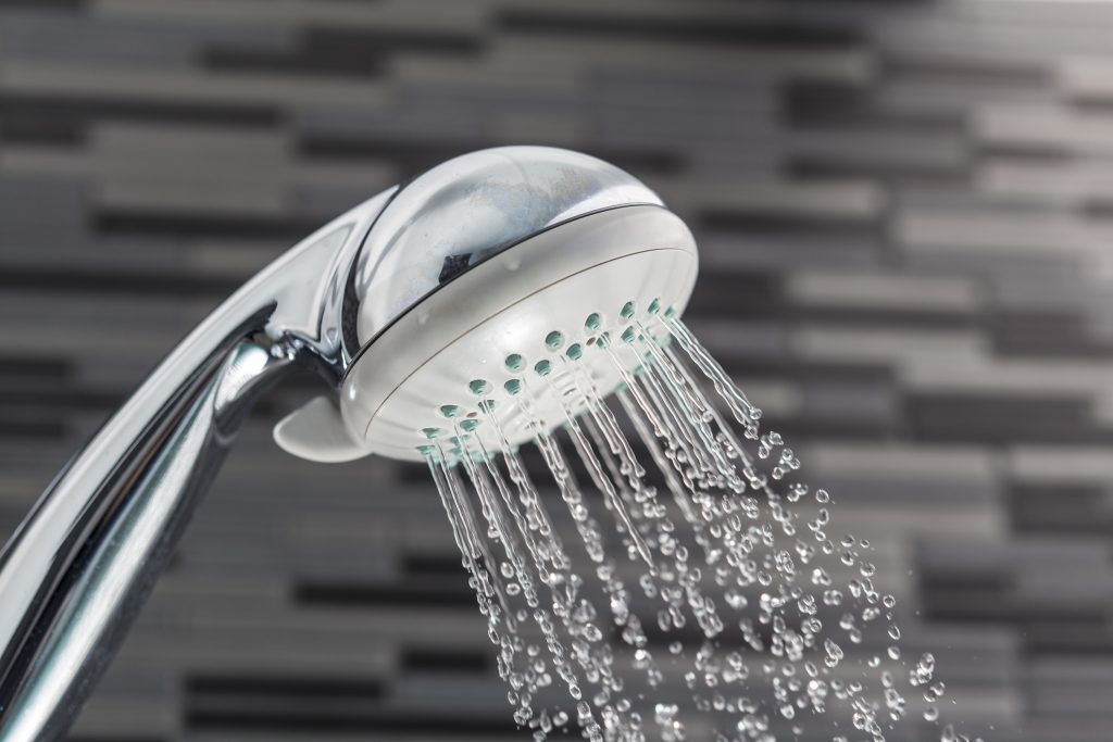 Silver shower head on a bathroom with water drops falling on a bathroom textured background