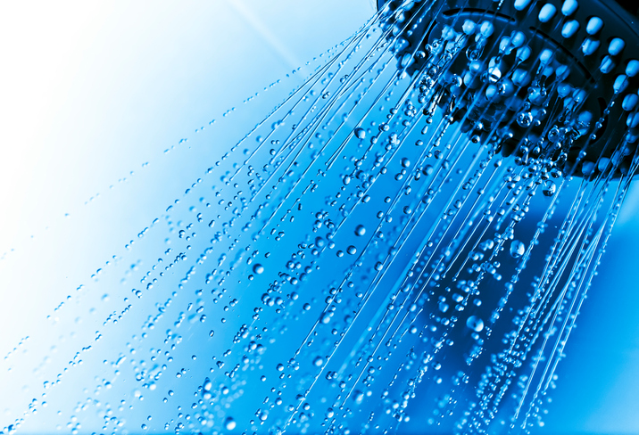 Shower head with running water showing drops and jets, against a blue and white tiled background