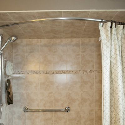 Beige tiled shower with two grab bars, hand shower and curved rod