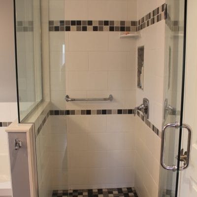 Glass shower with grab bar, mosaic tile bands and mosaic floor