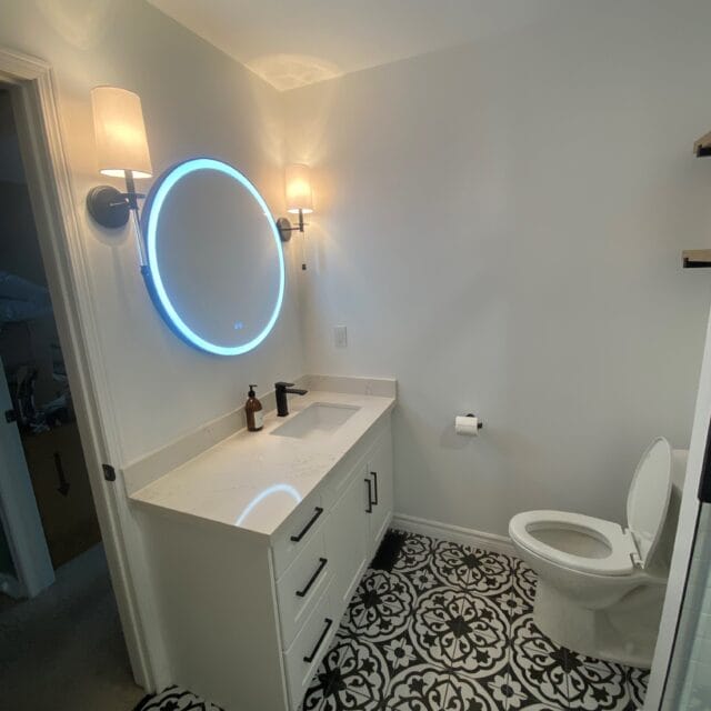 White vanity with a round lit mirror and patterned floor tile