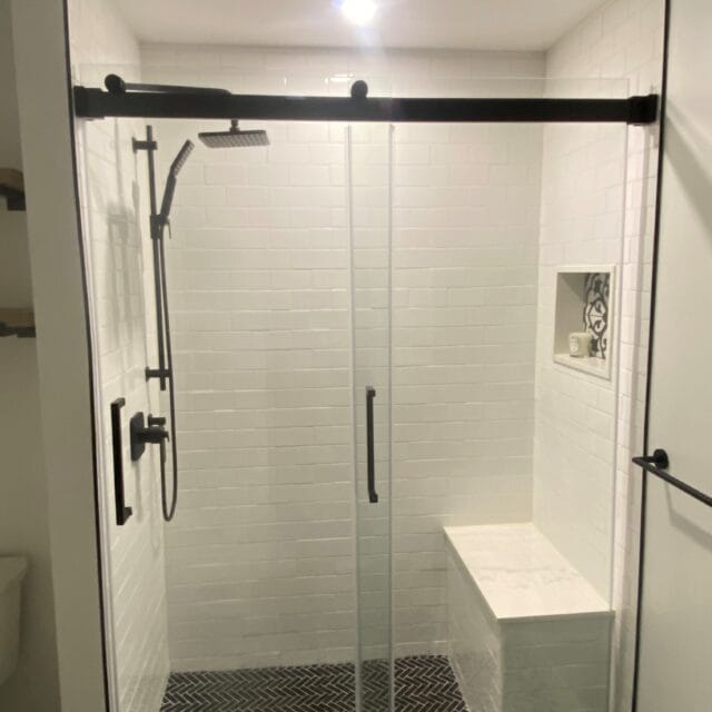 White subway tile shower with a sliding glass door, bench and niche