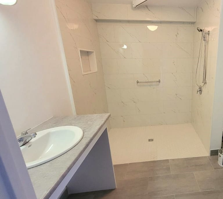 Curbless roll-in shower with a grab bar and hand shower beside an open roll-under vanity