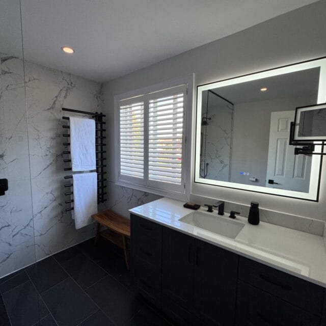 Renovated bathroom with a long vanity, lit mirror and walk-in shower