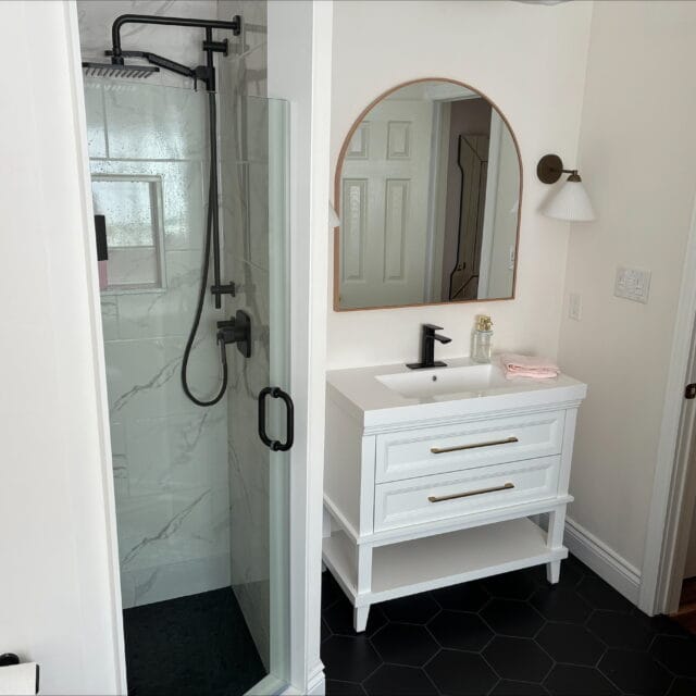 Glass shower beside a white vanity with an arched mirror